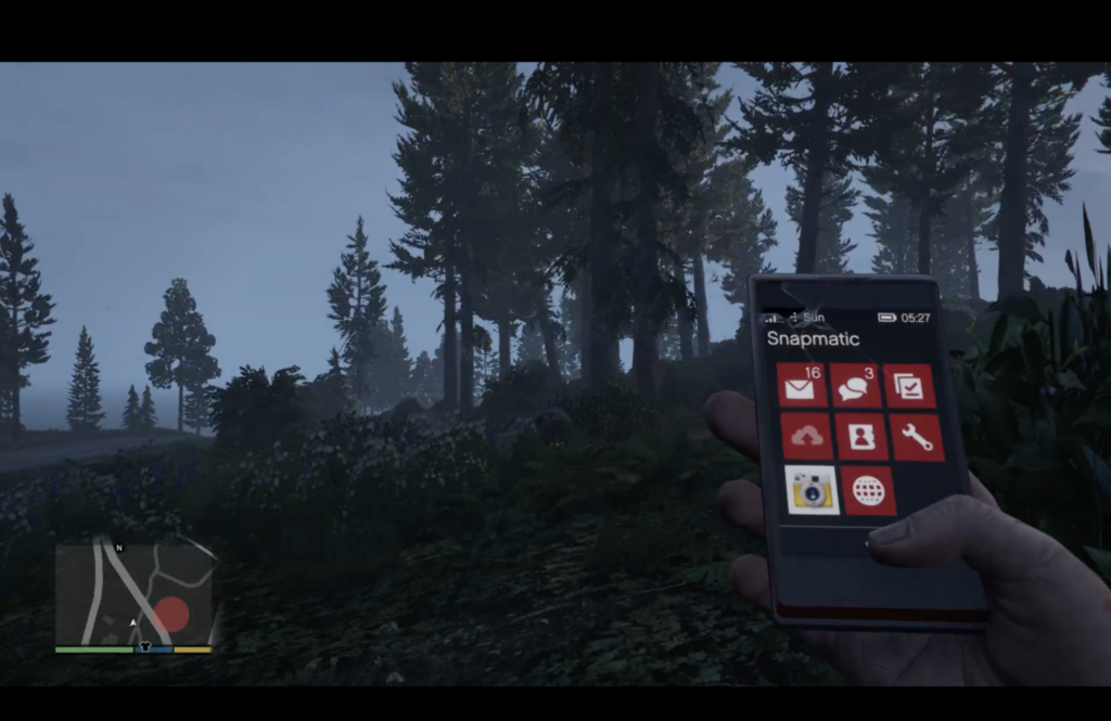 The image shows a screenshot from Grand Theft Auto V. From a first person perspective you look at a rural, forest area. The hand of your avatar holds a simulated smartphone showing a photo of the scene. 